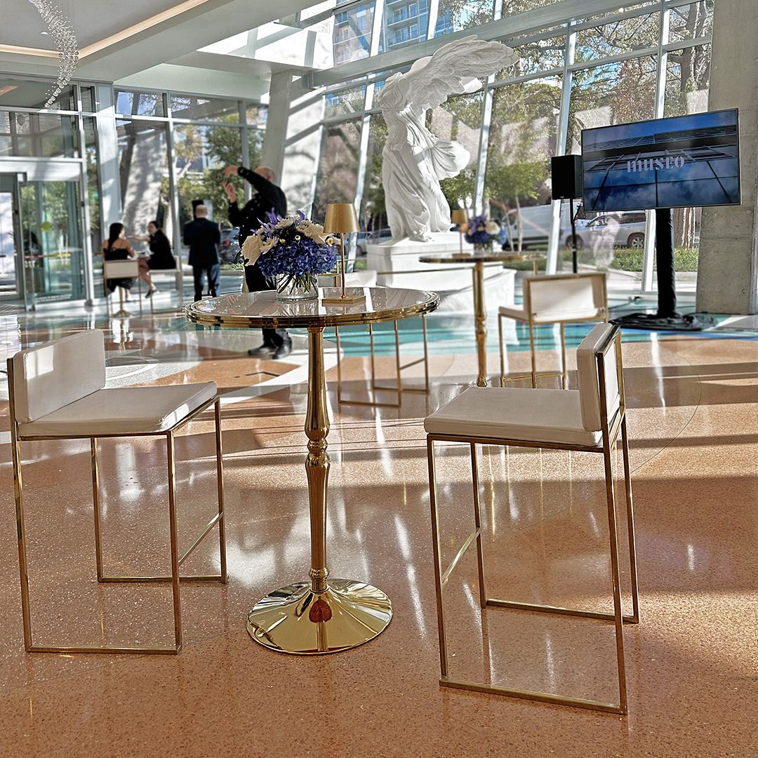 High cocktail tables arranged for a networking reception in the sunlit Museo lobby, featuring the Nike of Samothrace replica.