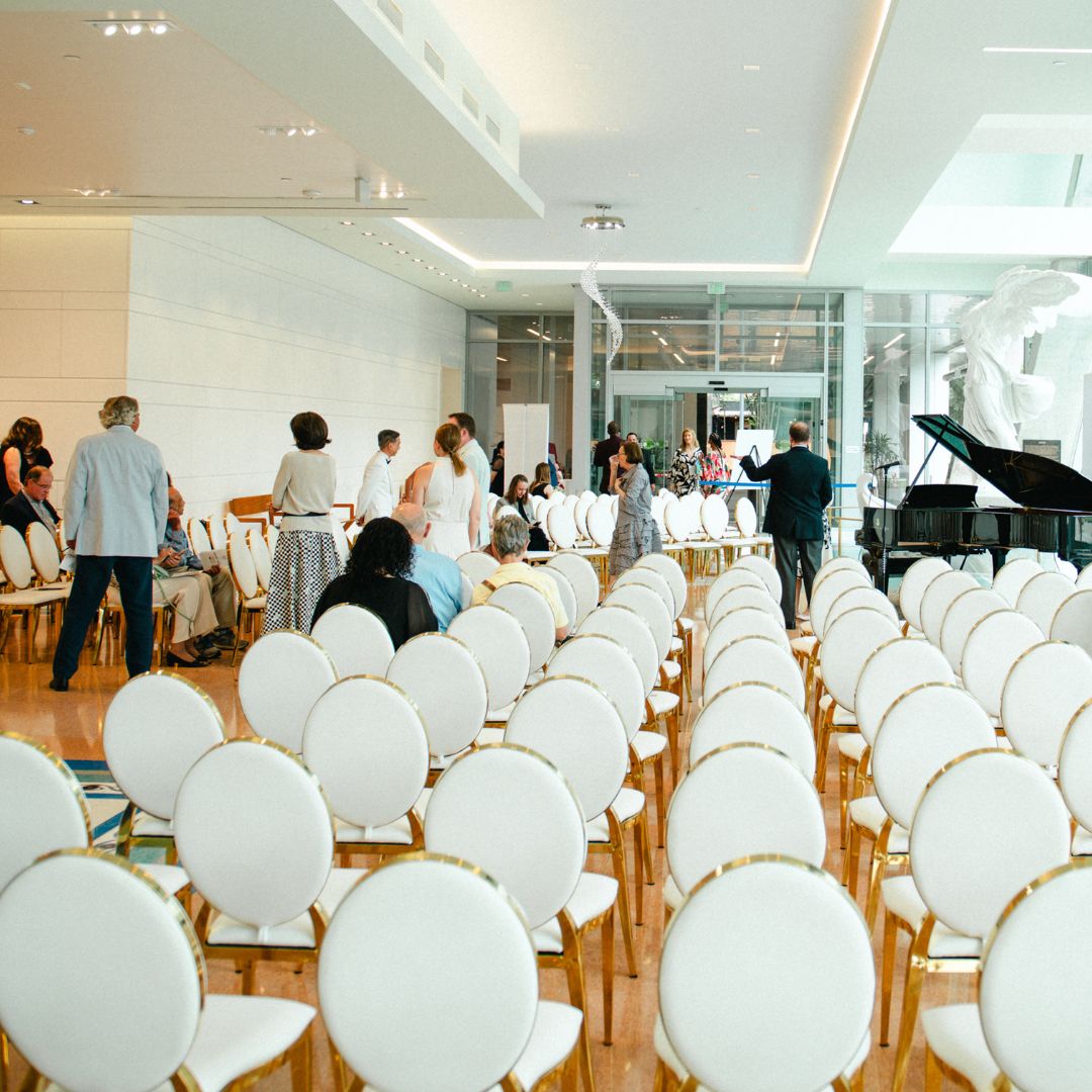 Rows of elegant white chairs arranged for a formal gathering or medical lecture in the bright, open hall of Museo Houston.
