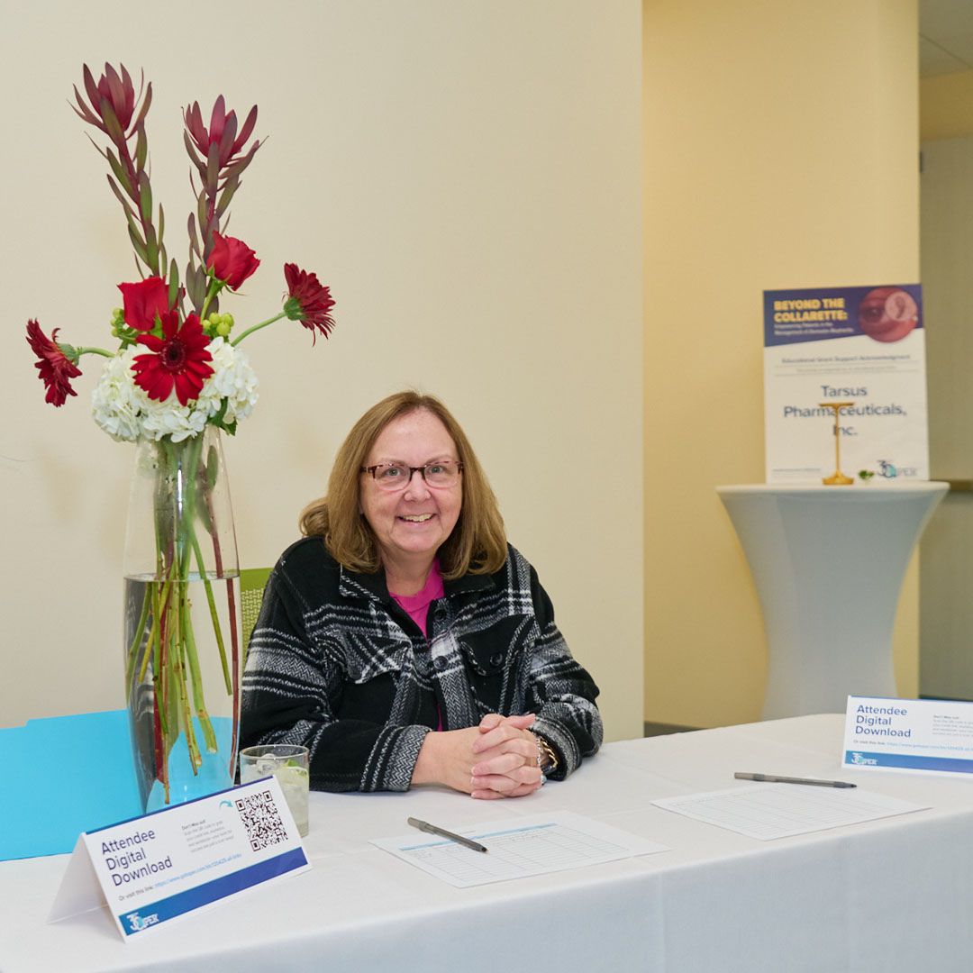 A staff member welcoming attendees at the floral-decorated registration desk for a Museo event.