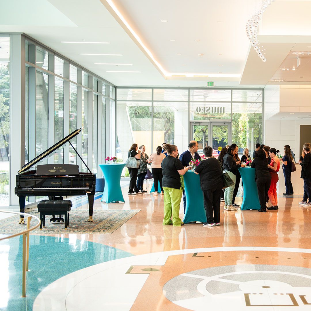 An elegant event setup at Museo Houston featuring high-top cocktail tables and a professional grand piano in a sun-drenched medical arts lobby.