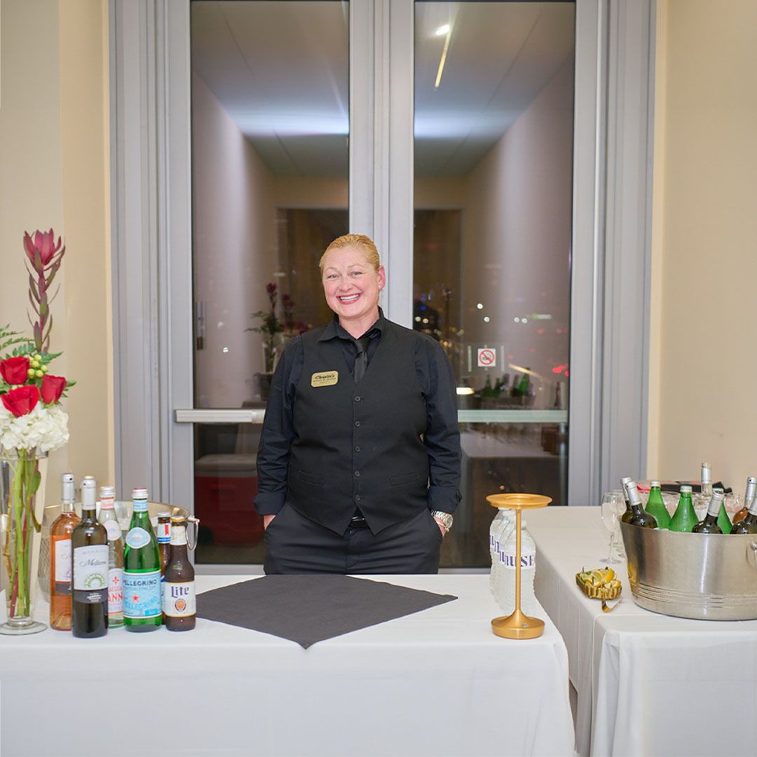 A friendly hospitality staff member standing behind a beautifully prepared refreshment station at Museo Houston.