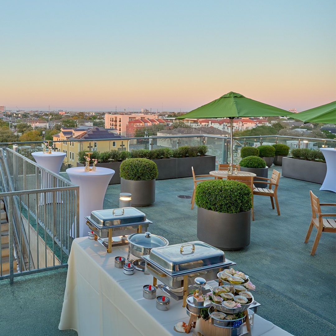 A professional catering buffet setup on the Museo Houston rooftop terrace prepared for an evening social gathering.