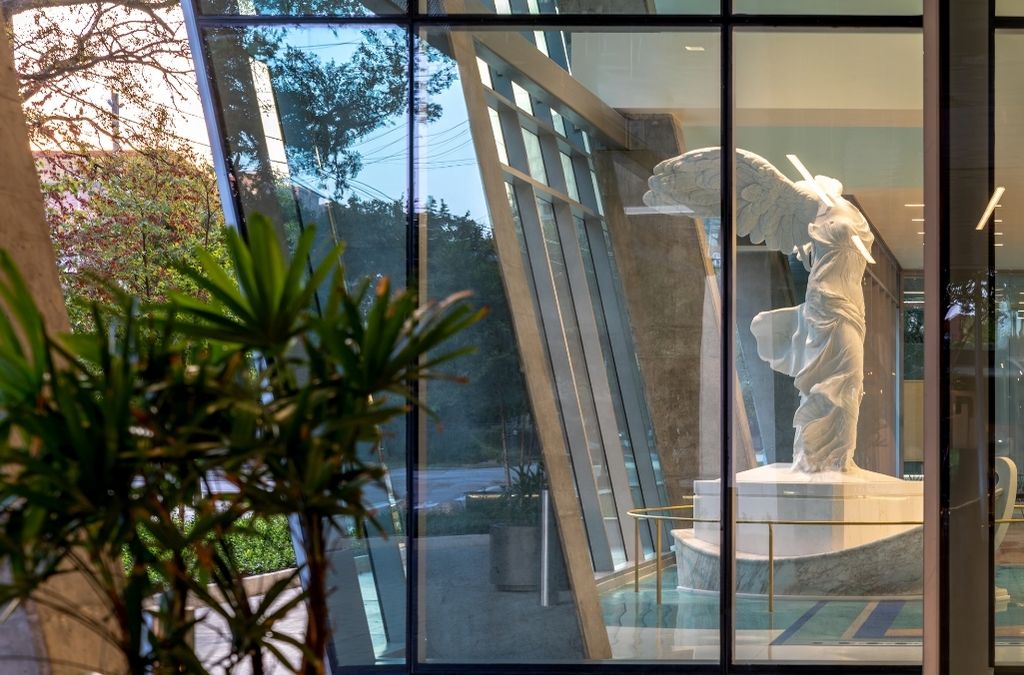 View of the classical Winged Victory statue looking through the exterior glass facade of Museo Houston.