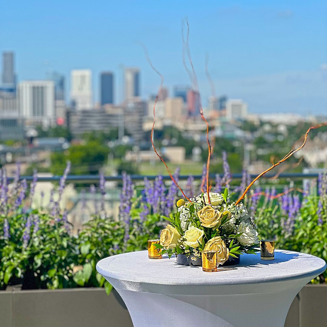 Beautiful floral arrangement on a cocktail table at the Museo rooftop garden, offering a panoramic daytime view of downtown Houston.