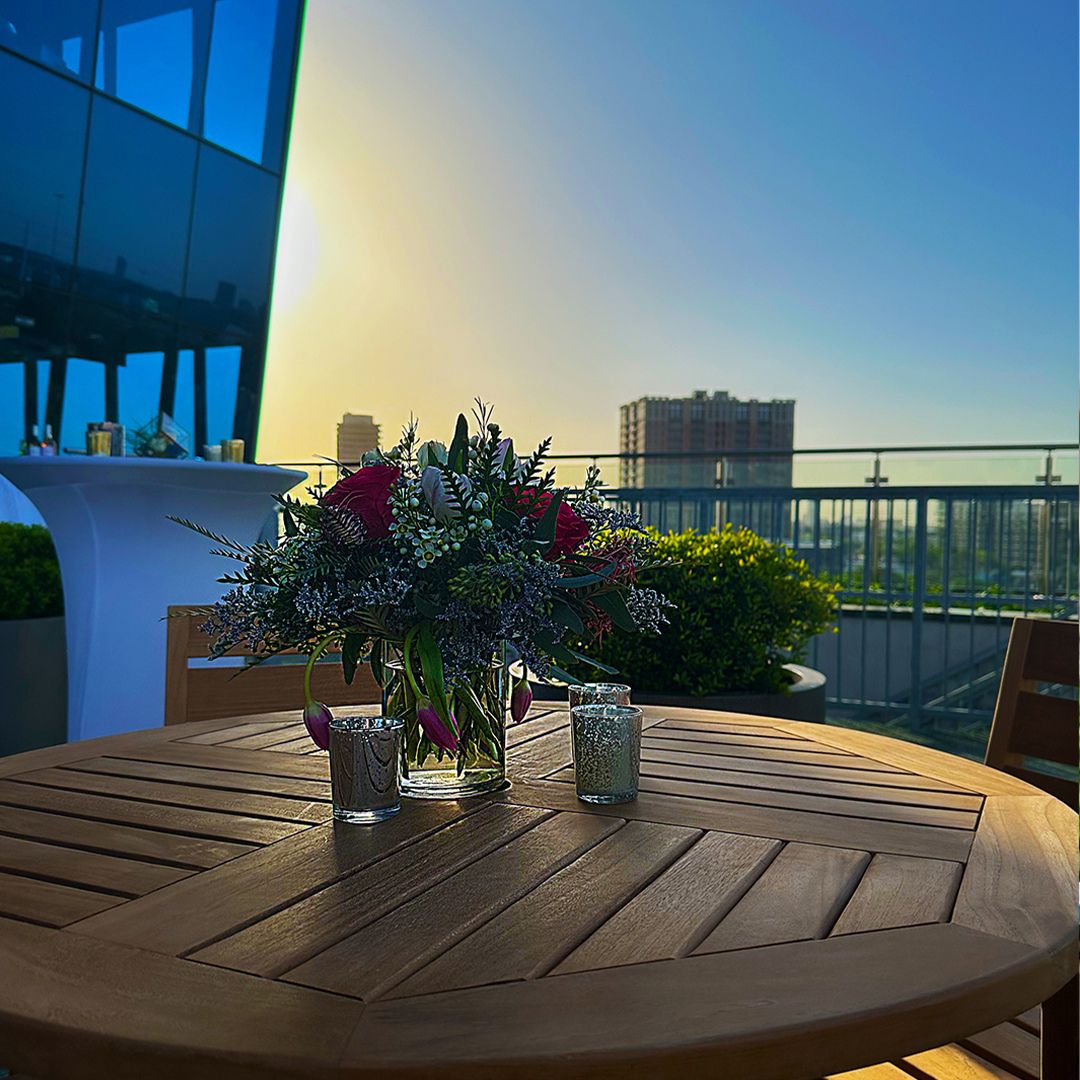 Elegant wooden table with a floral centerpiece on the Museo rooftop terrace at sunset, overlooking the beautiful Houston skyline.